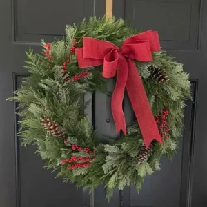 Handcrafted holiday wreath hanging on a black door with a red bow, berries, and pine cones