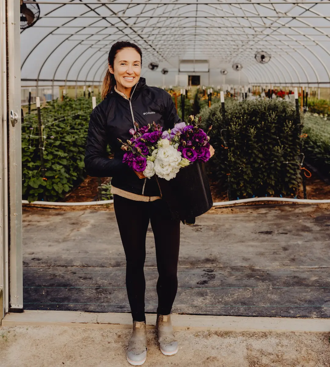 Dani Winters Founder of Winters Farm Florals standing in front of a hoop house with a bucket of grown flowers