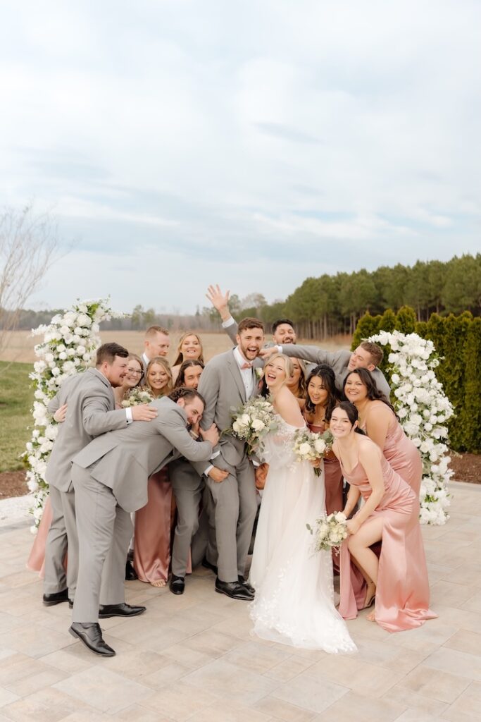 Bridal party laughing in front of white floral arches by Winters Farm Florals